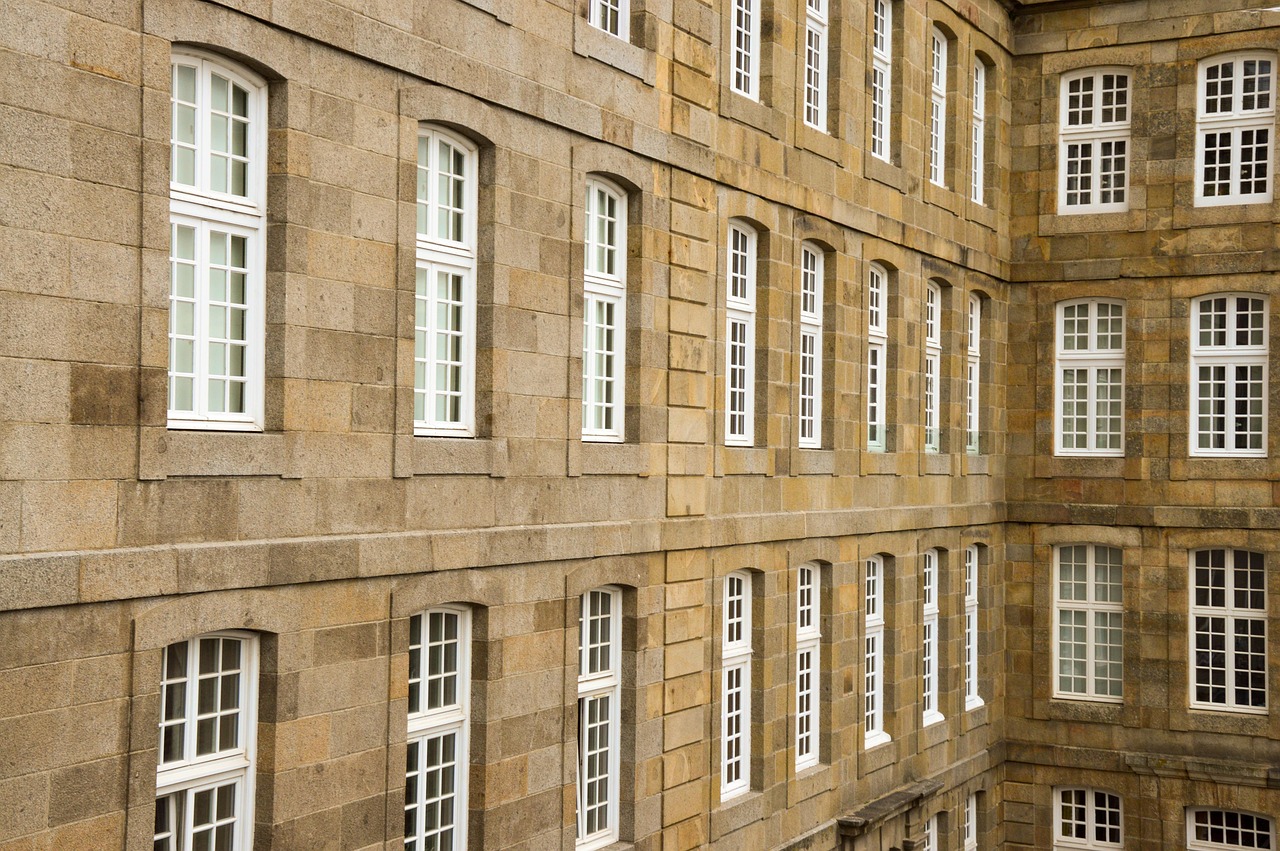 Façade massive en blocs de pierre de taille beige d'un bâtiment classique. On observe de nombreuses fenêtres blanches à petits carreaux, alignées de manière symétrique et répétitive sur plusieurs étages.