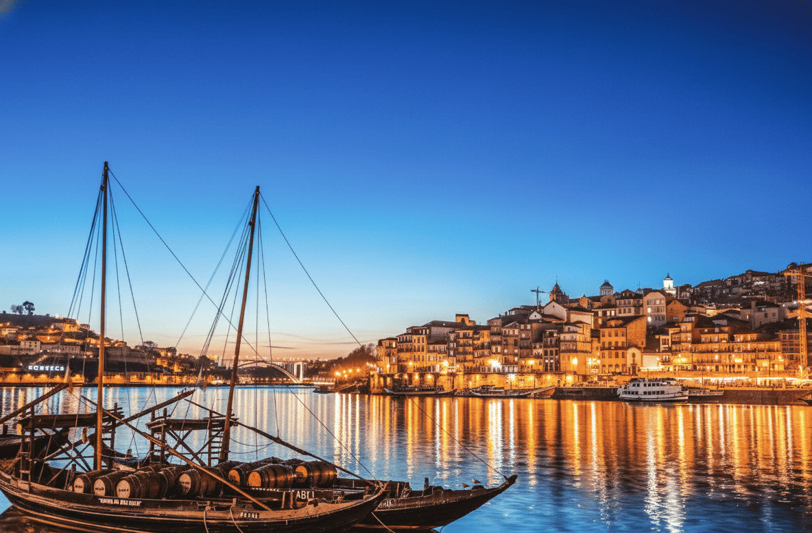 Bateaux traditionnels Rabelo sur le fleuve Douro à Porto, Portugal, au crépuscule. La rive de Vila Nova de Gaia est entièrement illuminée, reflétant les
